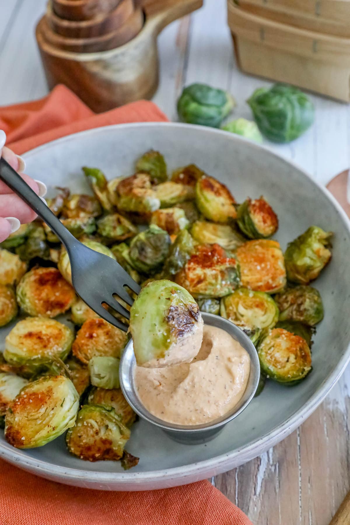 picture of garlic roasted brussels sprouts in a white bowl with a cup of sauce