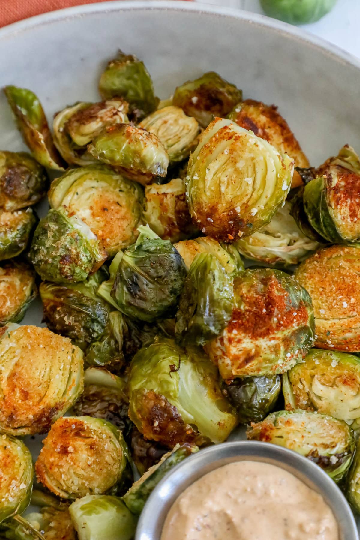 picture of garlic roasted brussels sprouts with seasoning in a white bowl with a cup of sauce