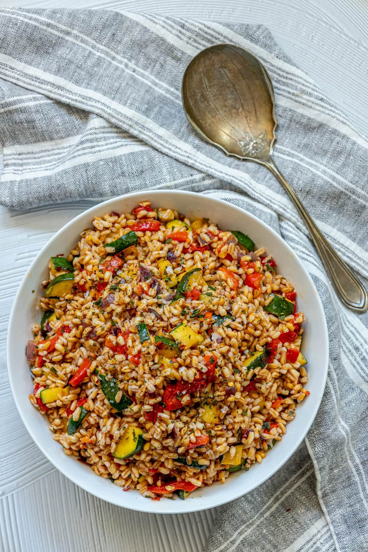 picture of farro salad in a white bowl with red peppers, zucchini, herbs, and shallots