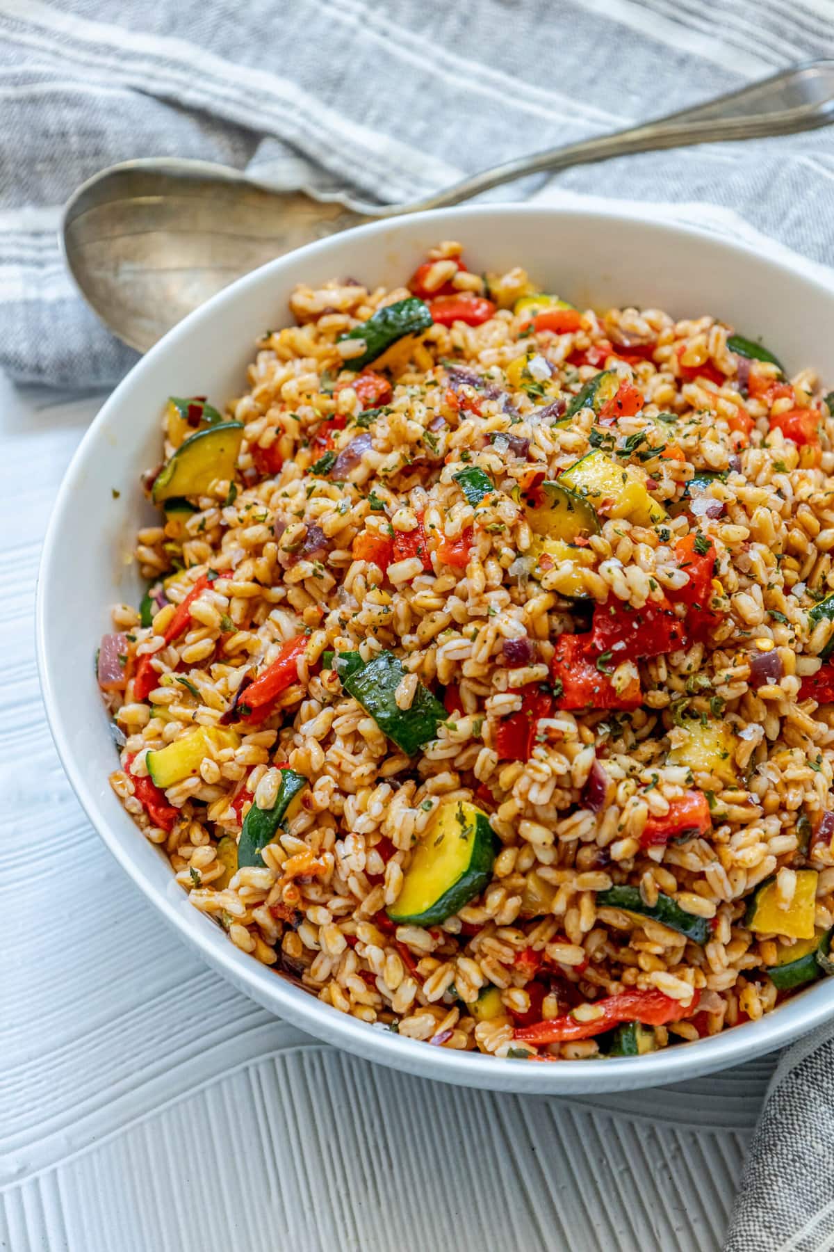 picture of farro salad in a white bowl with red peppers, zucchini, herbs, and shallots