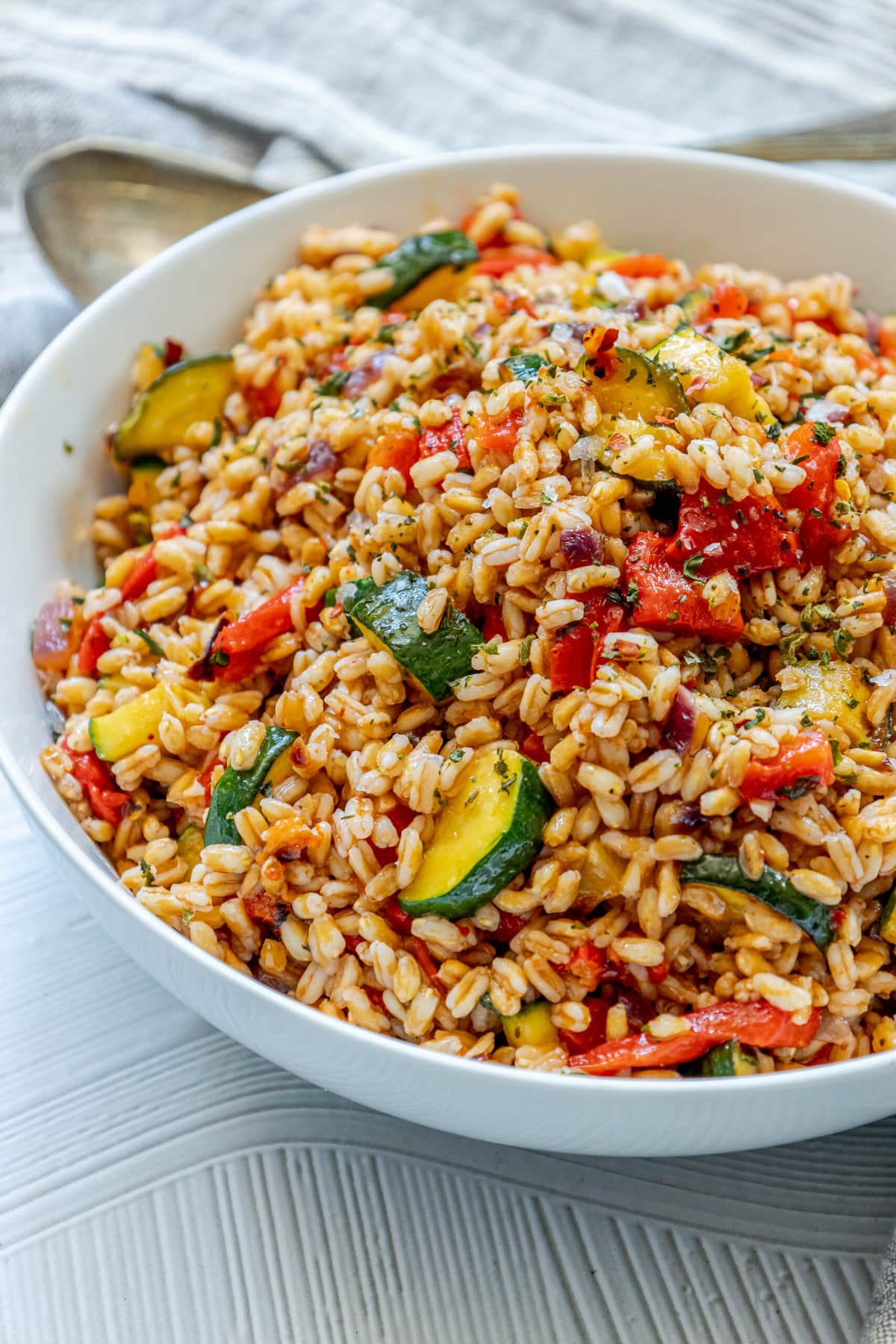 picture of farro salad with zucchini, red onion, red pepper, and herbs, in a white bowl on a table