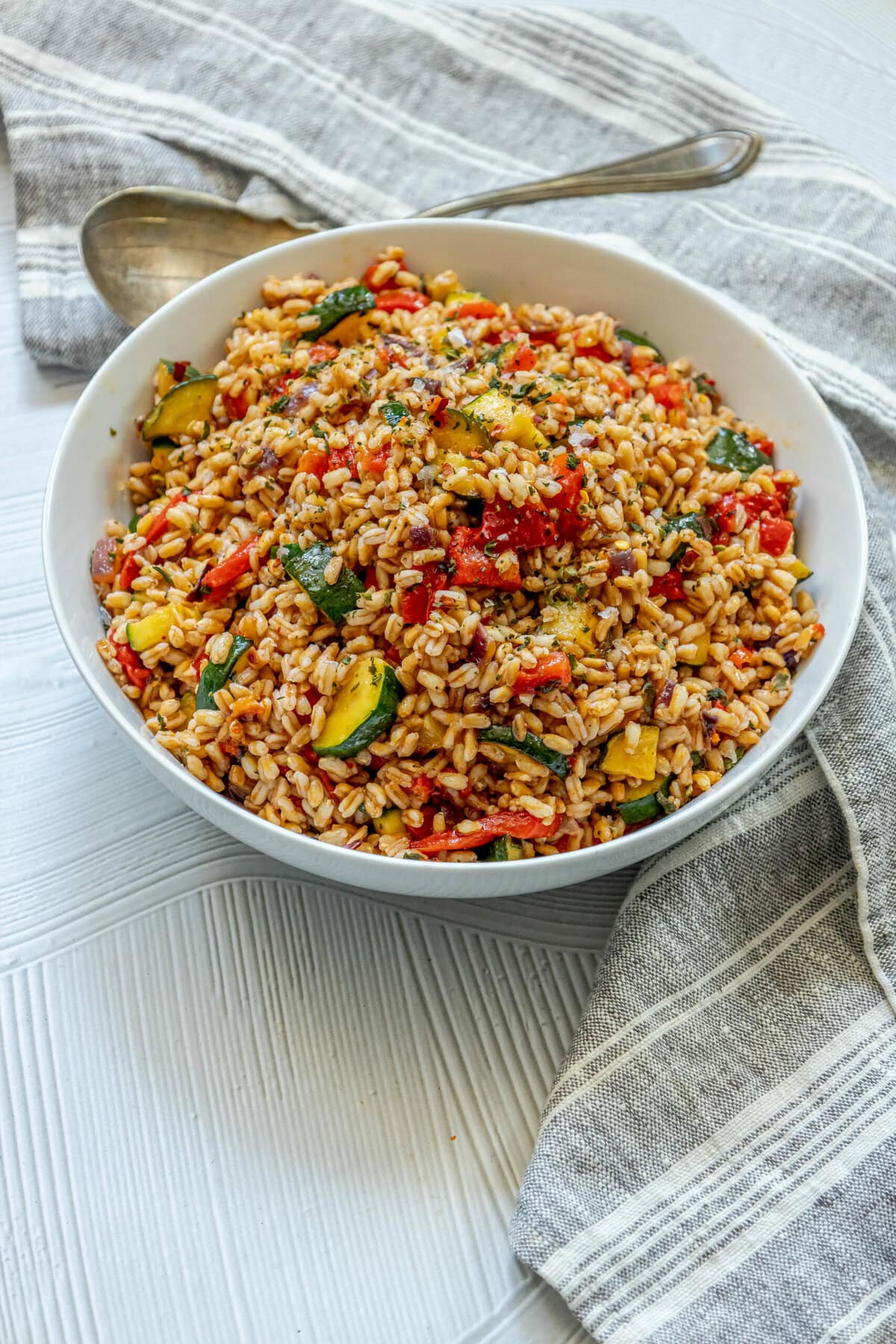 picture of farro salad in a white bowl with red peppers, zucchini, herbs, and shallots