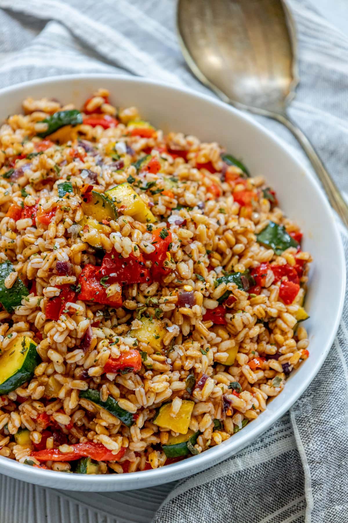 picture of farro salad in a white bowl with red peppers, zucchini, herbs, and shallots