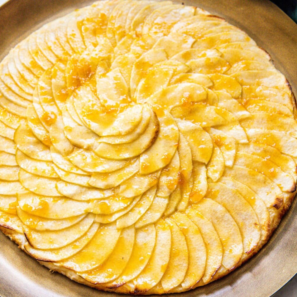 picture of a baked apple tart with thinly sliced apples baked in a circle and glazed with apricot glaze on a gold plate