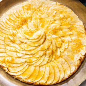 picture of a baked apple tart with thinly sliced apples baked in a circle and glazed with apricot glaze on a gold plate