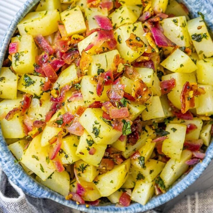 picture of german potato salad with red onions, herbs, and bacon on top in a blue bowl on a table