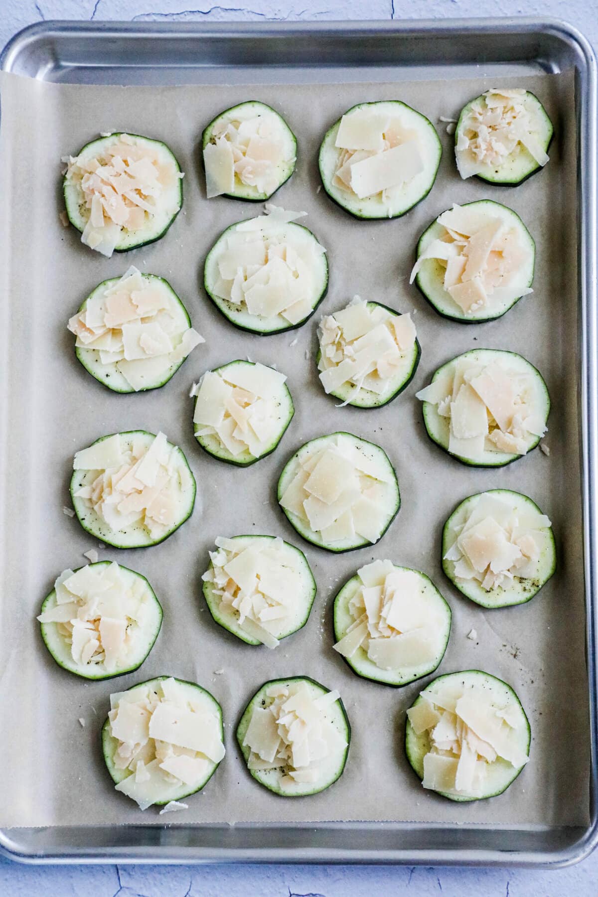 picture of sliced zucchini with seasonings and parmesan on a baking sheet lined with parchment paper