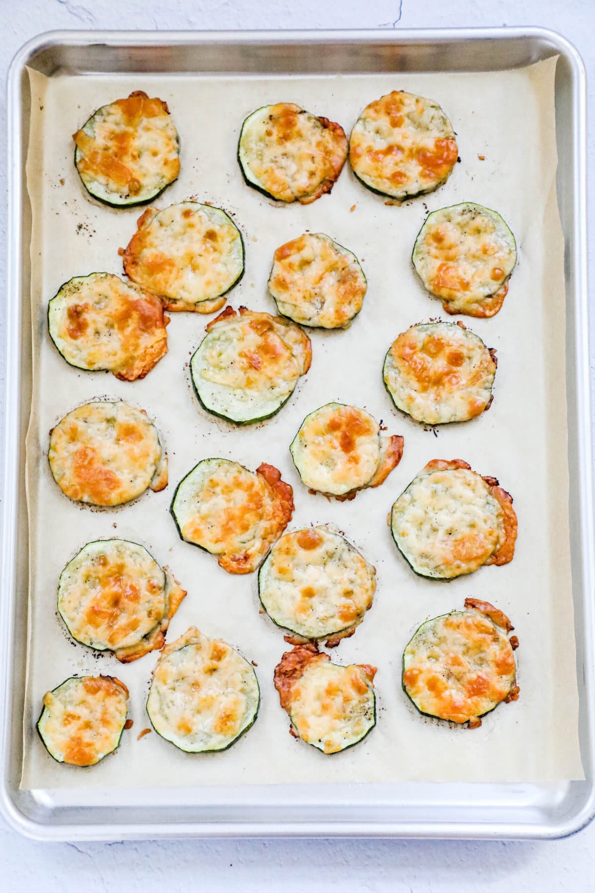 picture of baked sliced zucchini with melted cheese on a baking sheet lined with parchment paper