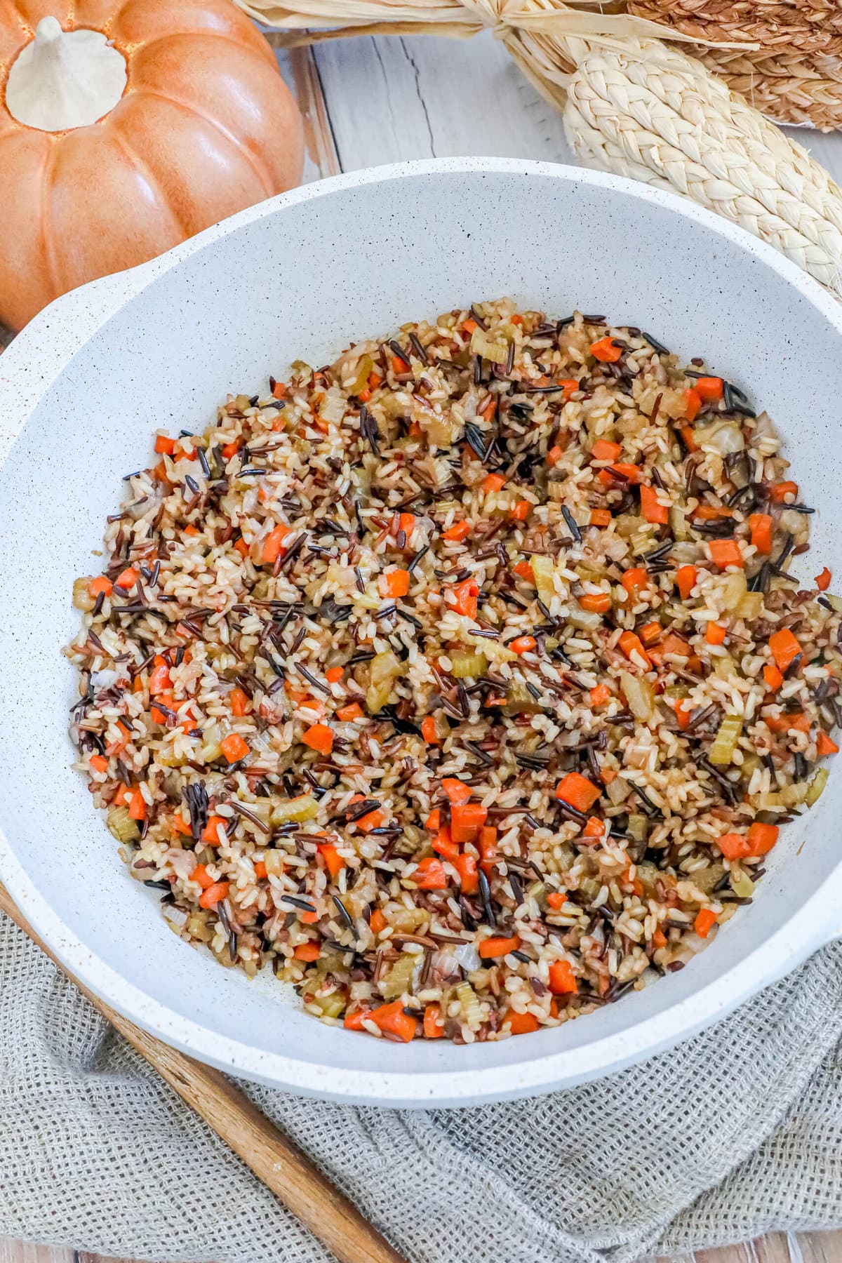 picture of wild rice pilaf in a white pan on a table with a wooden spoon sitting next to it 