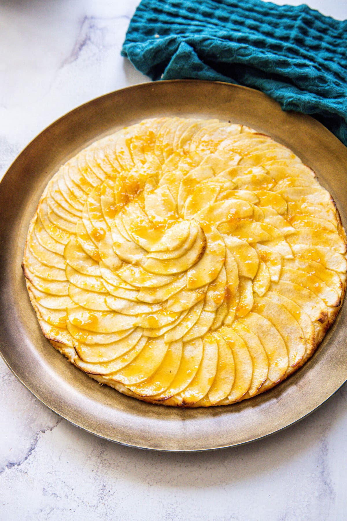 picture of a baked apple tart with thinly sliced apples baked in a circle and glazed with apricot glaze on a gold plate