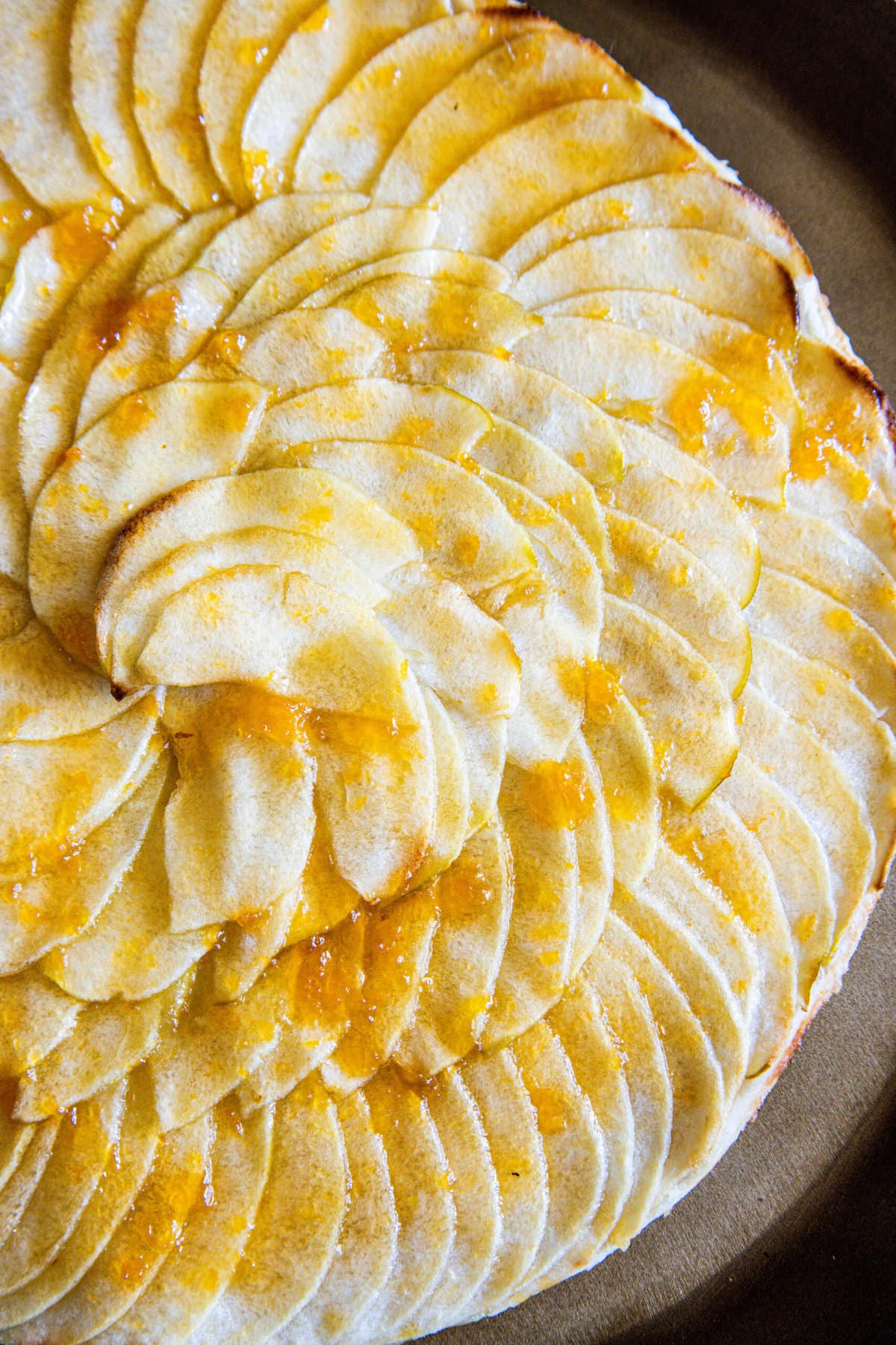 picture of a baked apple tart with thinly sliced apples baked in a circle and glazed with apricot glaze on a gold plate