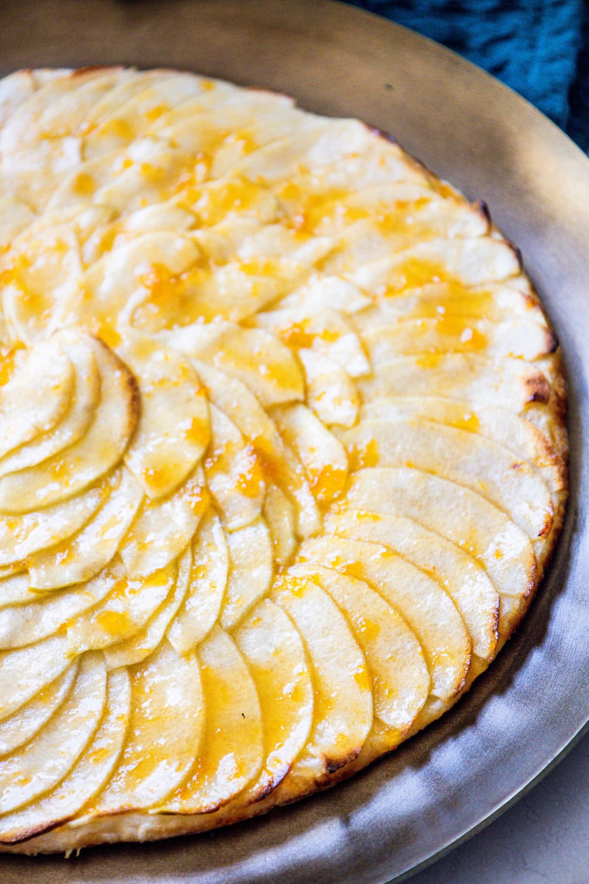 picture of a baked apple tart with thinly sliced apples baked in a circle and glazed with apricot glaze on a gold plate