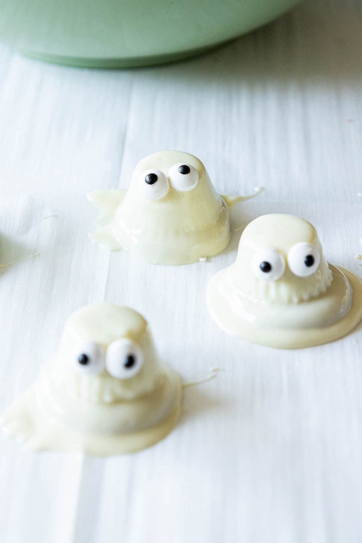 picture of dipped white chocolate ghosts setting on parchment paper on baking sheet