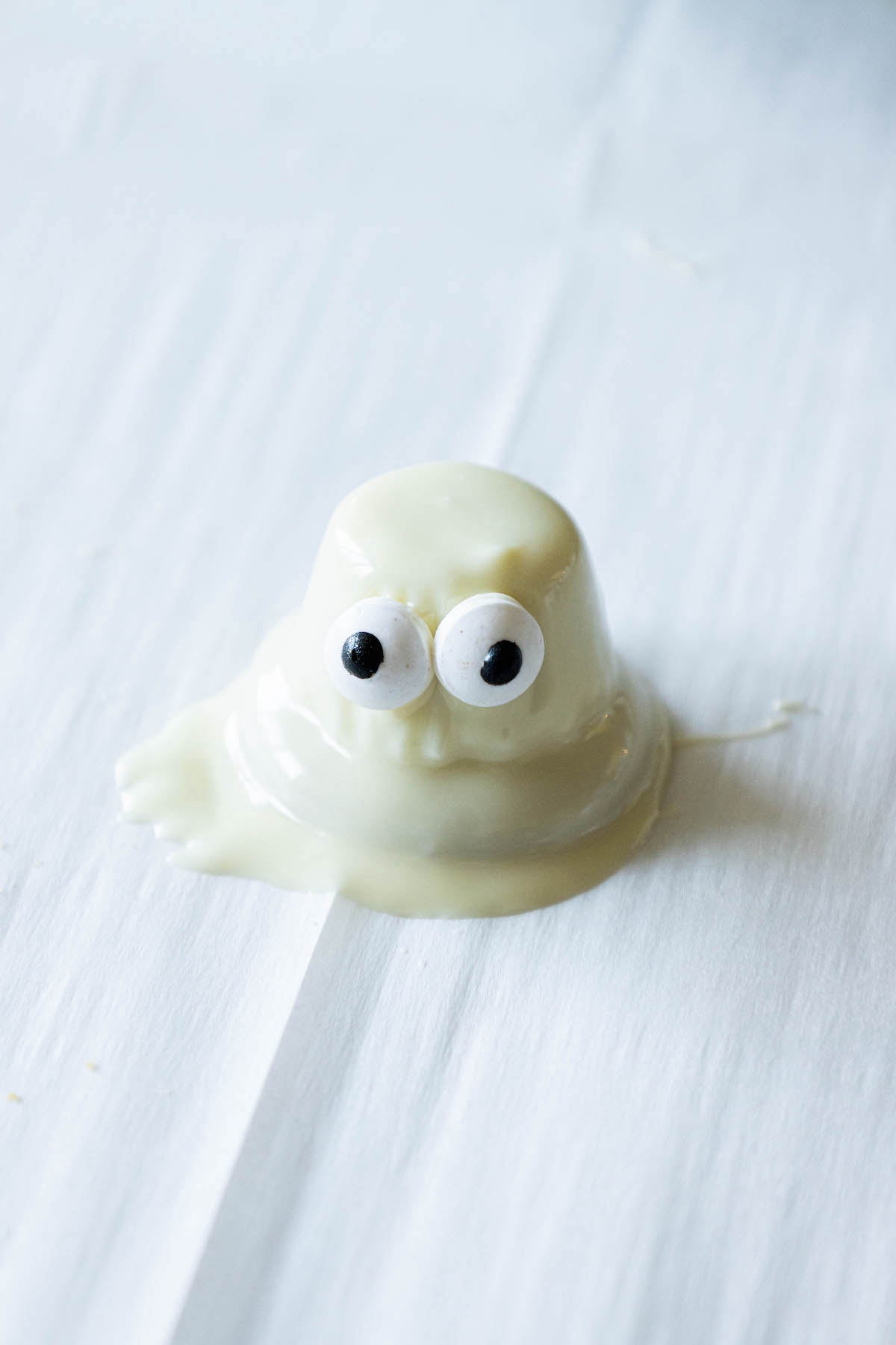 picture of dipped white chocolate ghost cookie setting on a baking sheet lined with parchment paper with candy eyes affixed to it