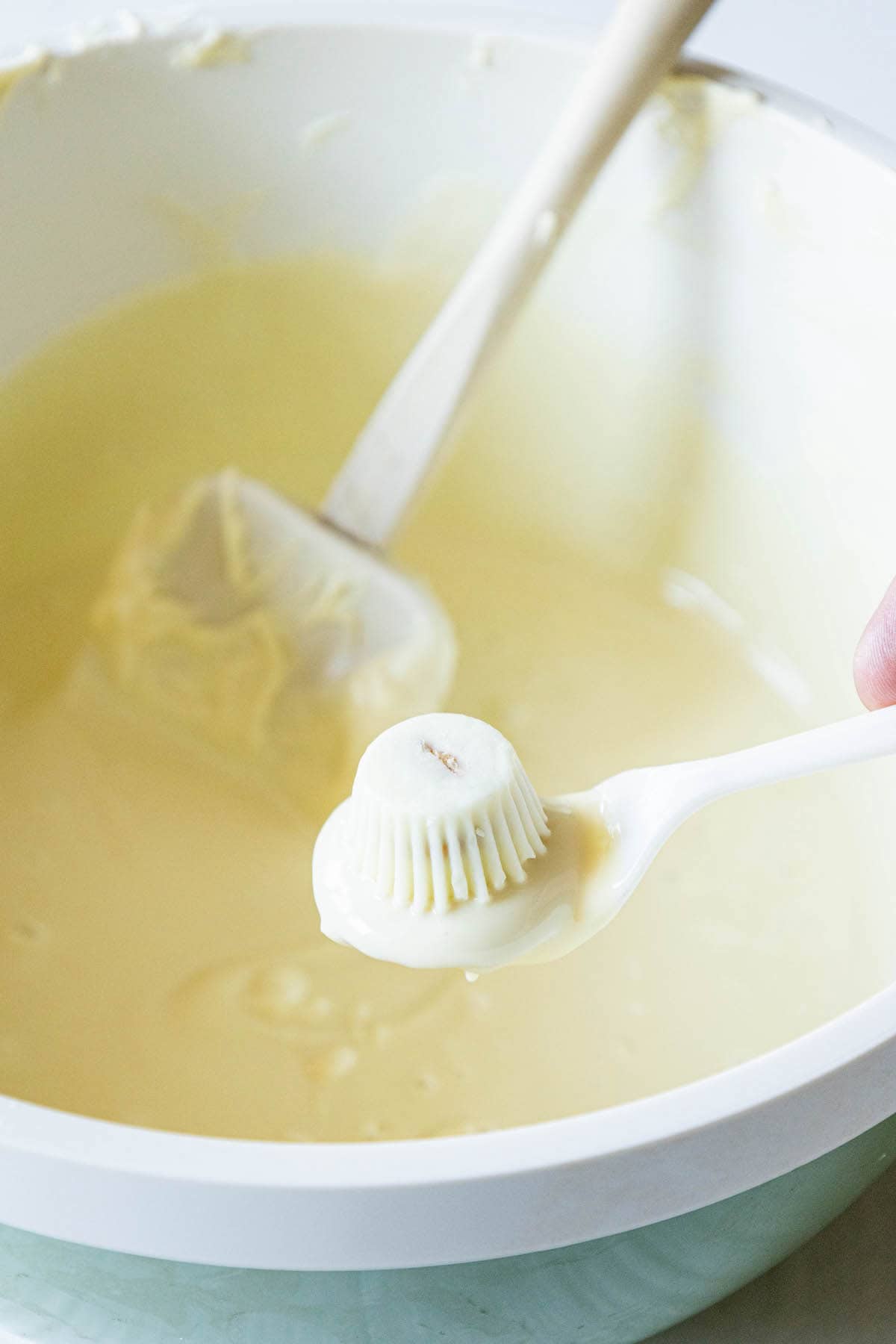 picture of a golden oreo on a spoon dipped in white chocolate with a white chocolate reeses peanut butter cup on top about to be dipped in a bowl of melted white chocolate