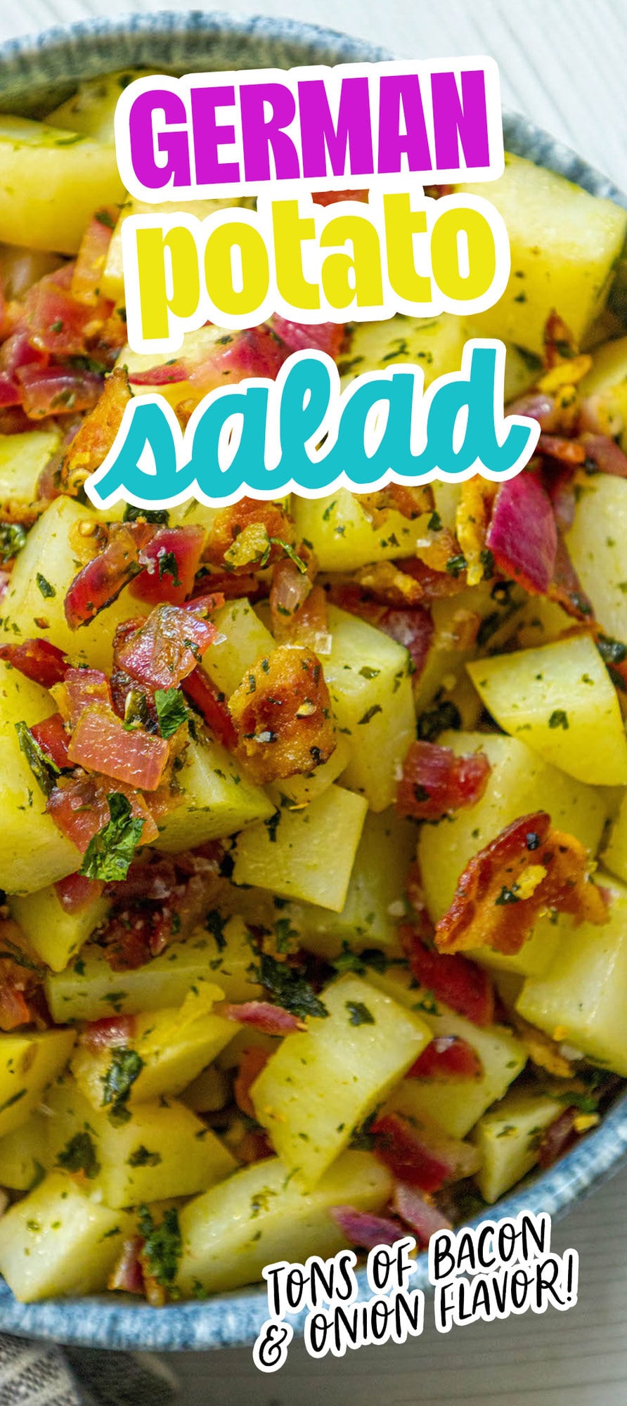 picture of german potato salad with red onions, herbs, and bacon on top in a blue bowl on a table