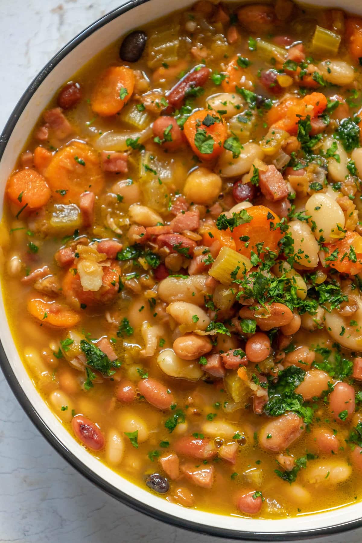 picture of soup in a bowl with ham, beans, celery, and parsley on top 