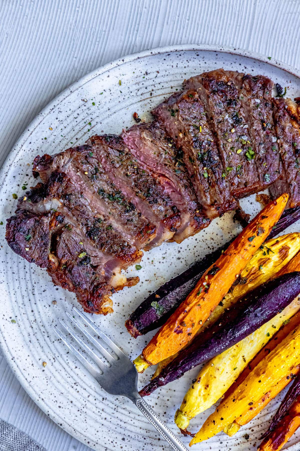 picture of a grilled steak sliced into strips and seasoned with salt, pepper, and herbs on a plate