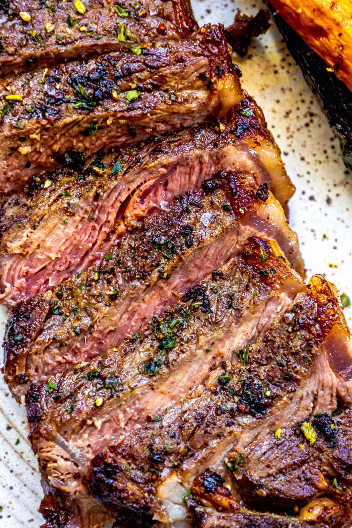 picture of a grilled steak sliced into strips and seasoned with salt, pepper, and herbs on a plate