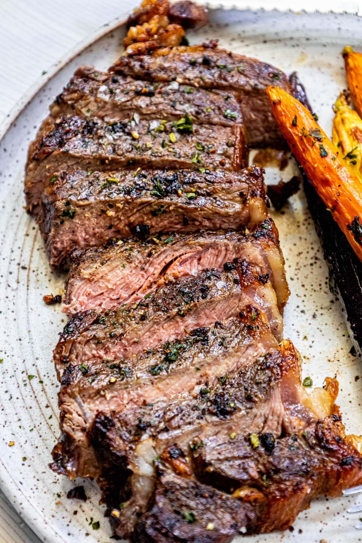 picture of a grilled steak sliced into strips and seasoned with salt, pepper, and herbs on a plate