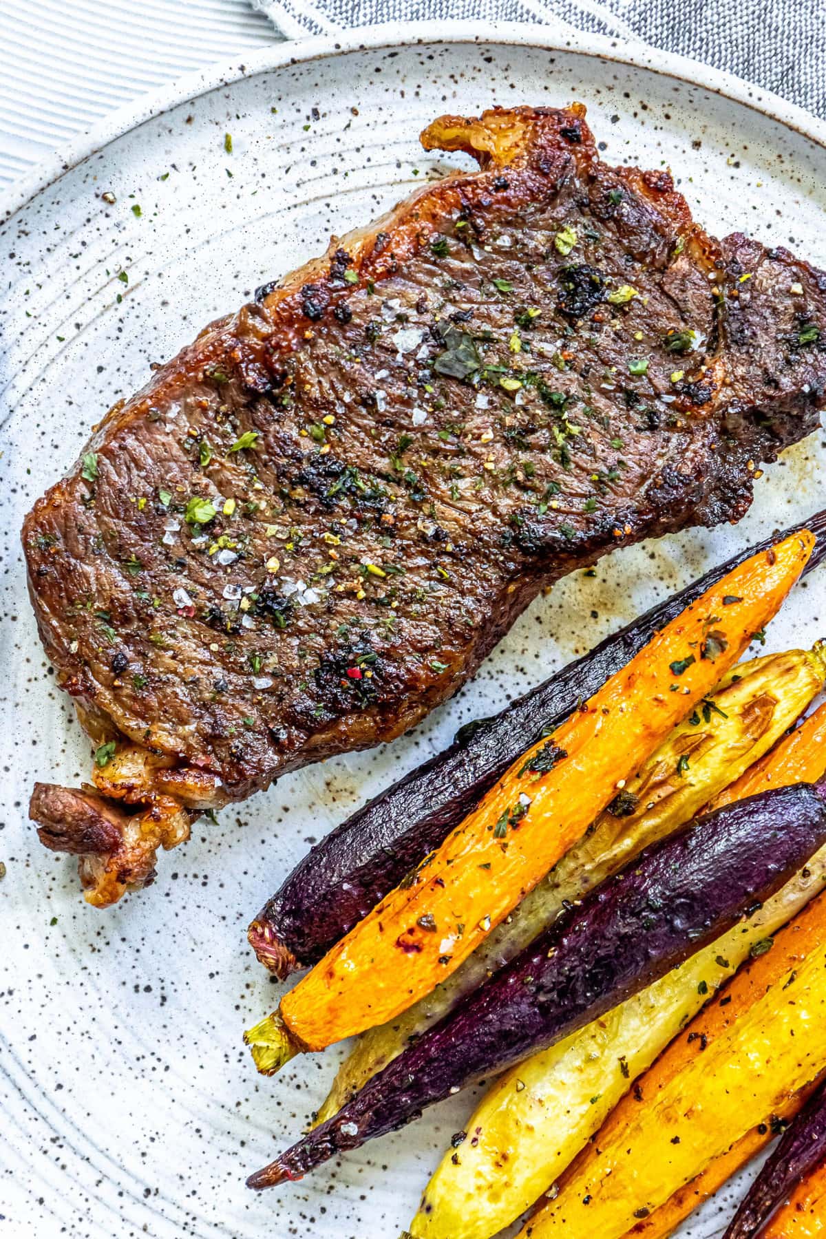 picture of a grilled steak seasoned with salt, pepper, and herbs on a plate