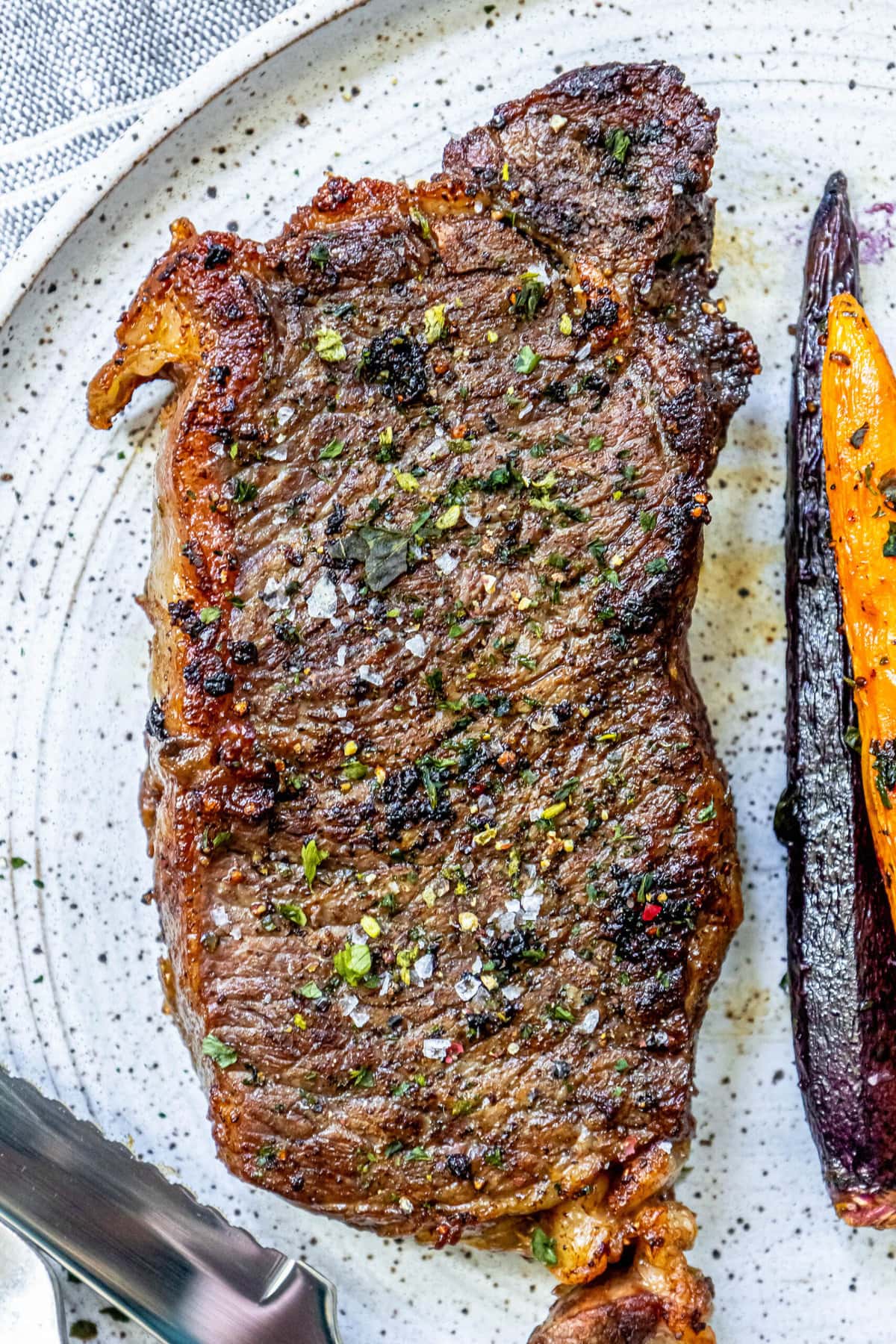 picture of a grilled steak seasoned with salt, pepper, and herbs on a plate
