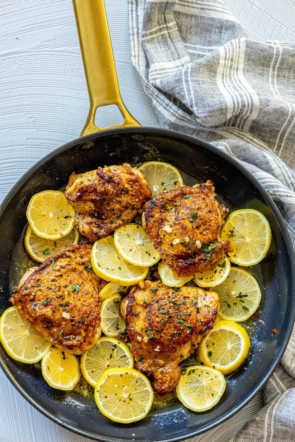 picture of seared chicken thigh in a pan seasoned with garlic herbs and lemon slices