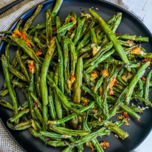 picture of roasted green beans with parmesan and bread crumbs on a black plate