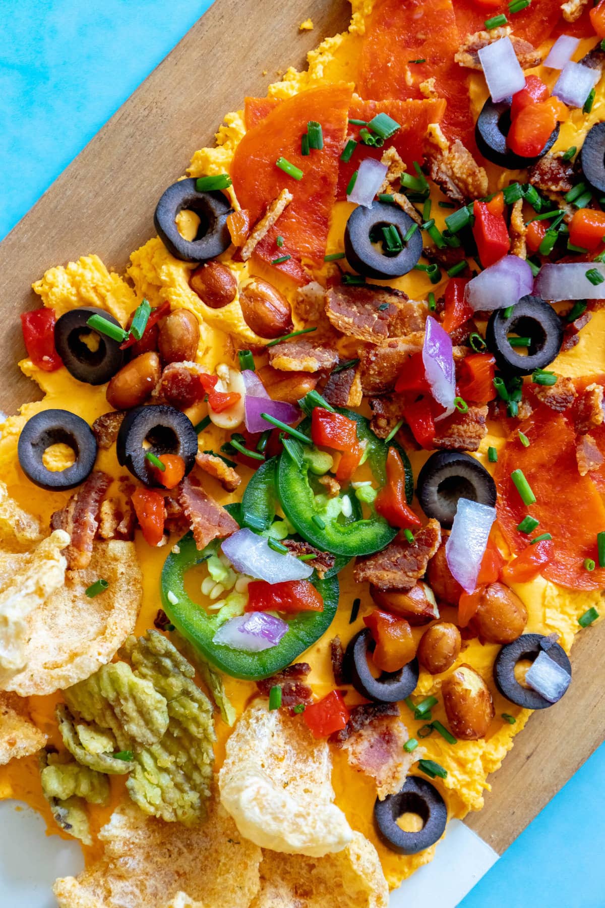 picture of pub cheese spread on a board covered with pork rinds, jalapenos, olives, bacon crumbles, peanuts, pimiento peppers, chives, red onion, and pepperoni