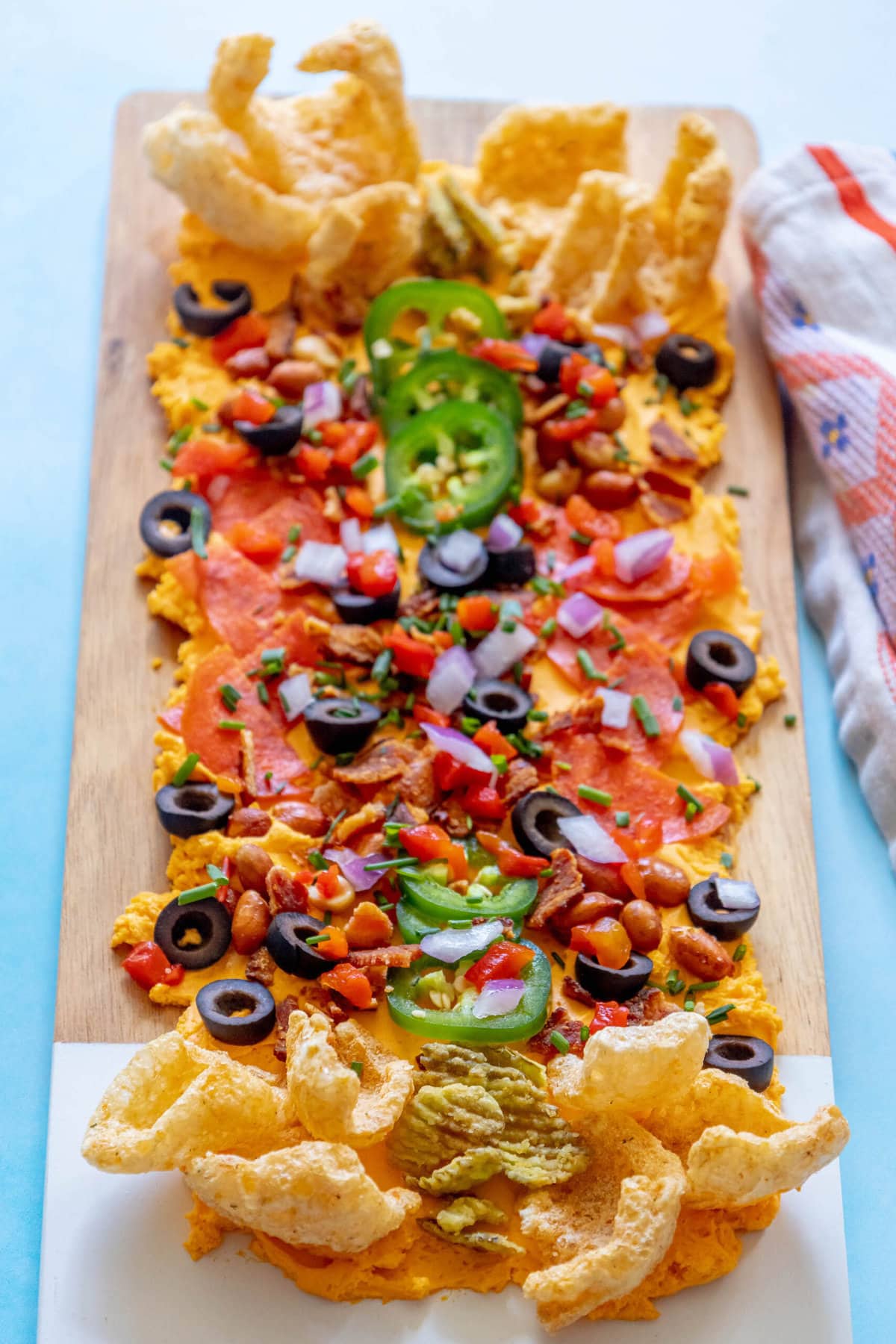 picture of pub cheese spread on a board covered with pork rinds, jalapenos, olives, bacon crumbles, peanuts, pimiento peppers, chives, red onion, and pepperoni