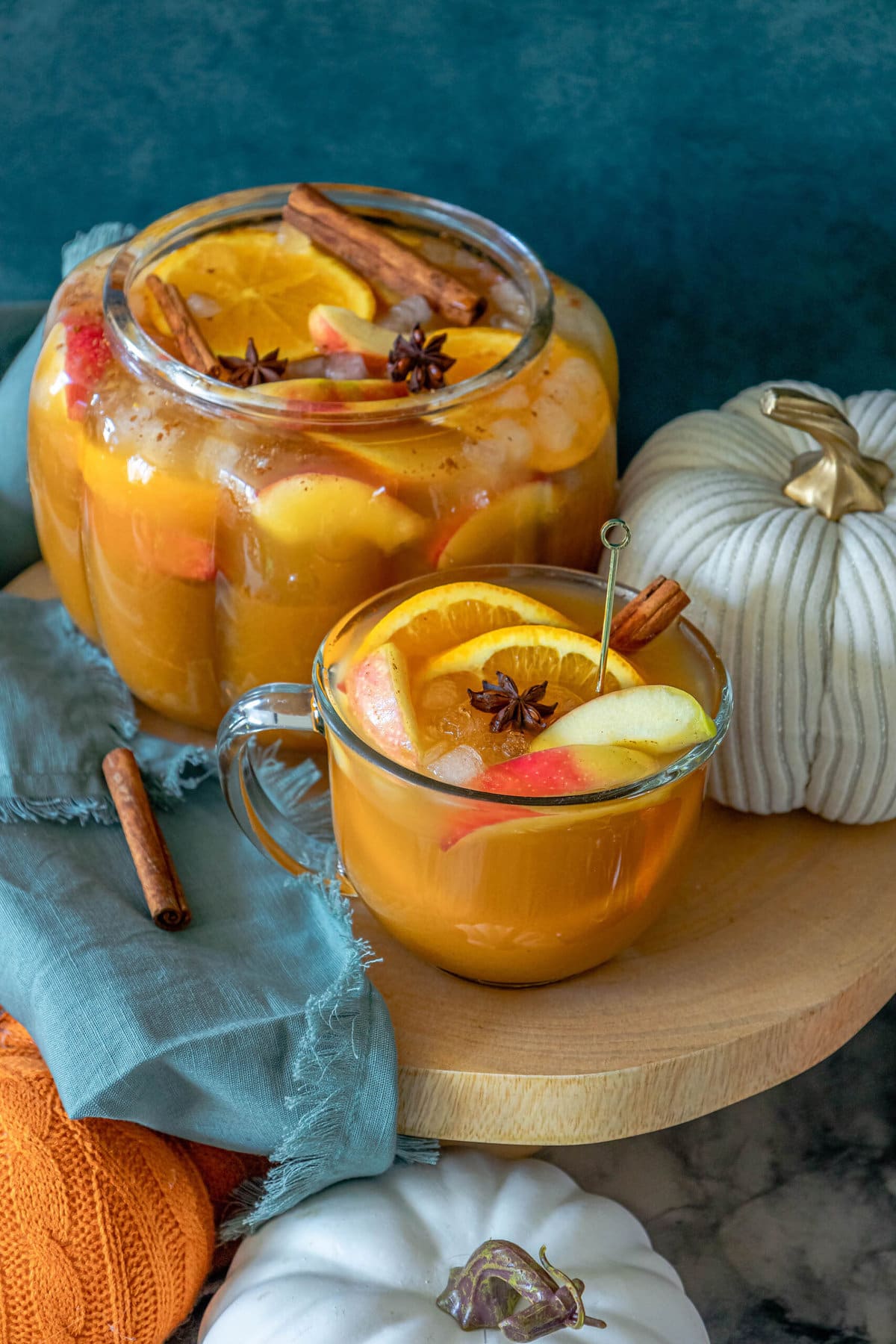 pumpkin punch in a clear mug with orange slices, apple slices, cinnamon stick, ice cubes, and a star of anise in it