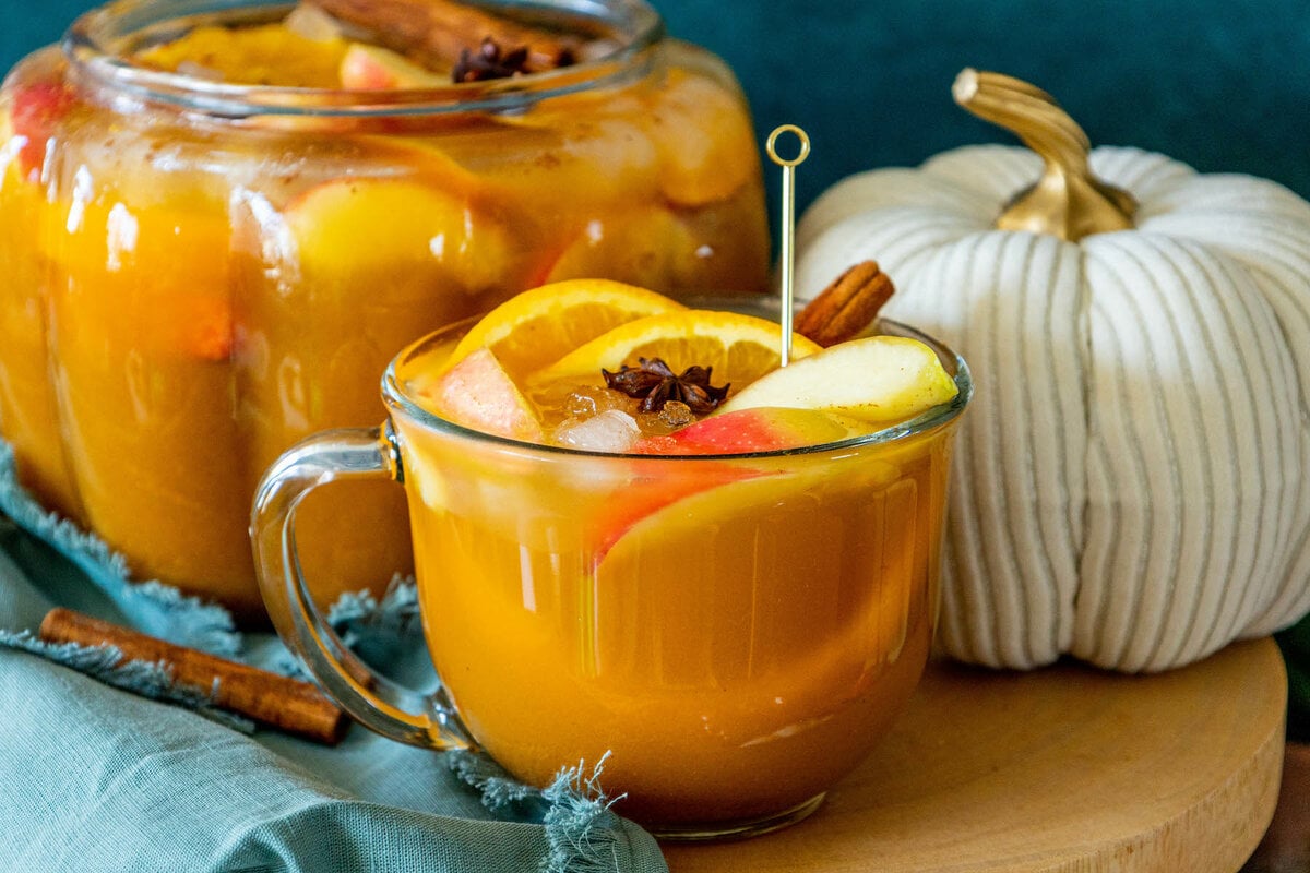 picture of pumpkin punch in a clear mug with orange slices, apple slices, cinnamon stick, ice cubes, and a star of anise in it