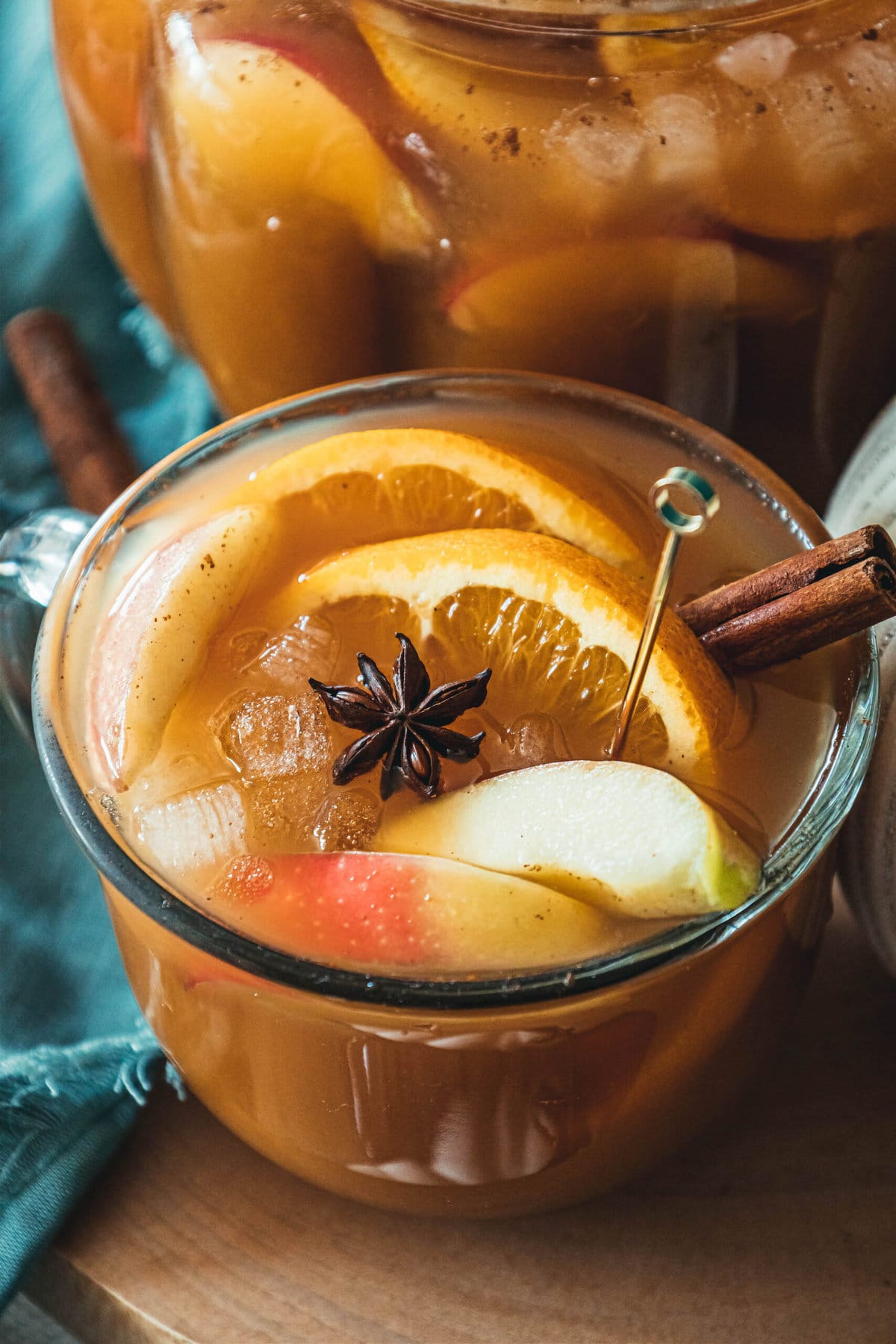 picture of pumpkin punch in a clear mug with orange slices, apple slices, cinnamon stick, ice cubes, and a star of anise in it