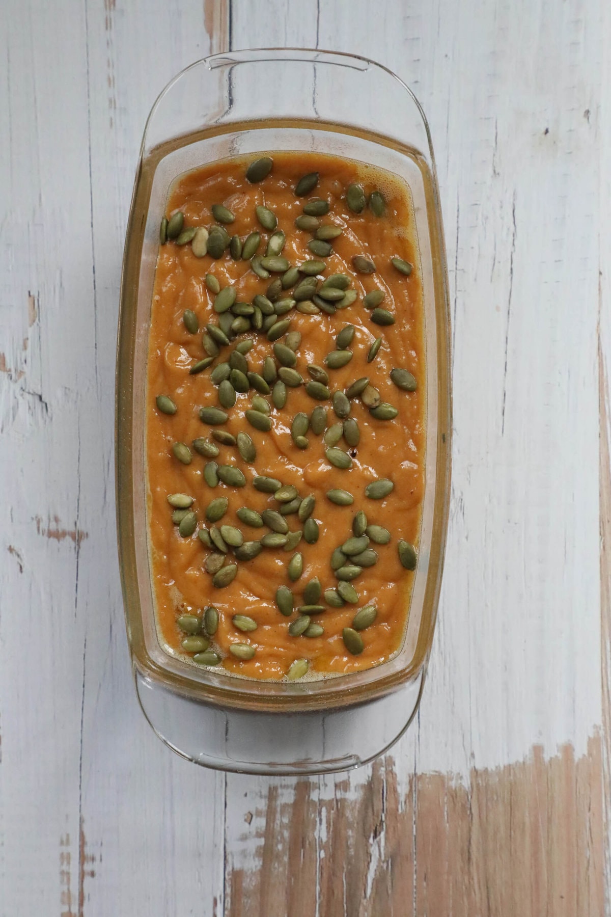 A glass dish with pumpkin seeds for a pumpkin loaf recipe.