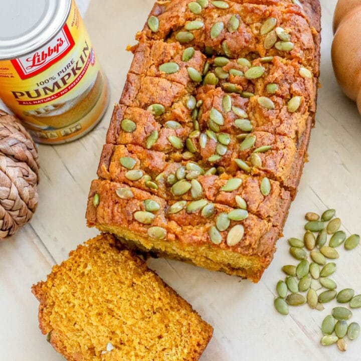 picture of pumpkin bread with pumpkin seeds baked onto the top sliced on a table