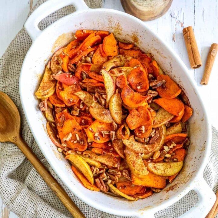 picture of baked cinnamon apples and sweet potatoes in a white baking dish with a spoon on a table