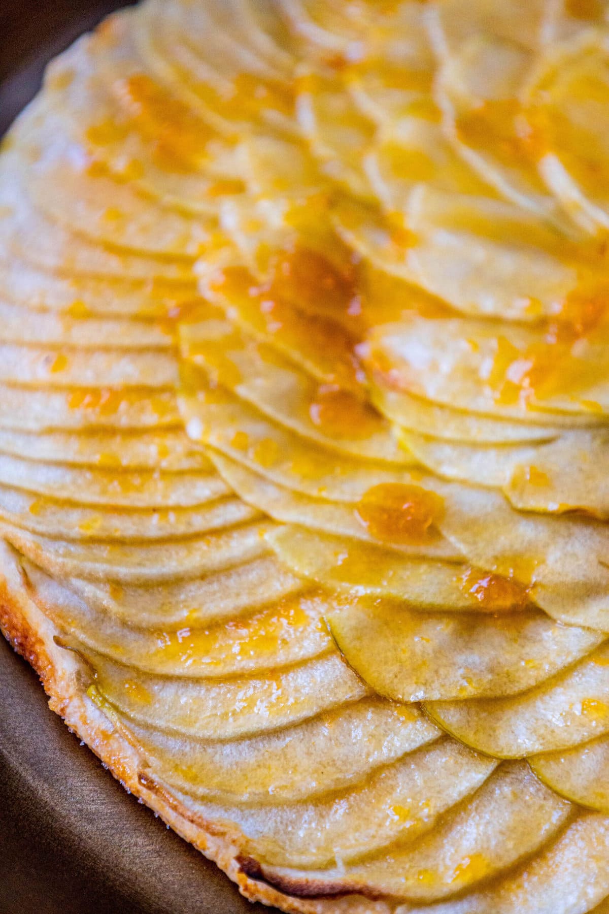 picture of a baked apple tart with thinly sliced apples baked in a circle and glazed with apricot glaze on a gold plate