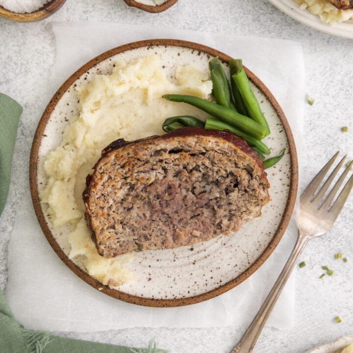meatloaf on a white plate with mashed potatoes and green beans