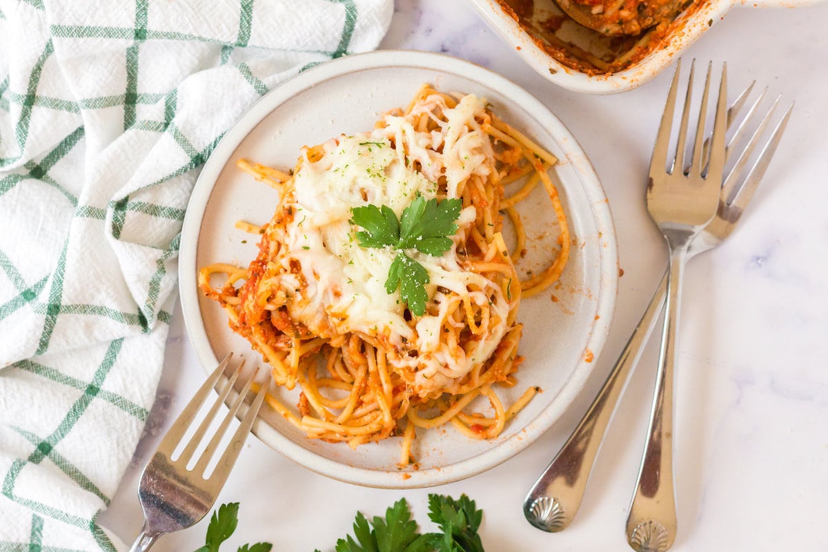 picture of baked spaghetti with melted cheese on a plate topped with basil with forks next to it