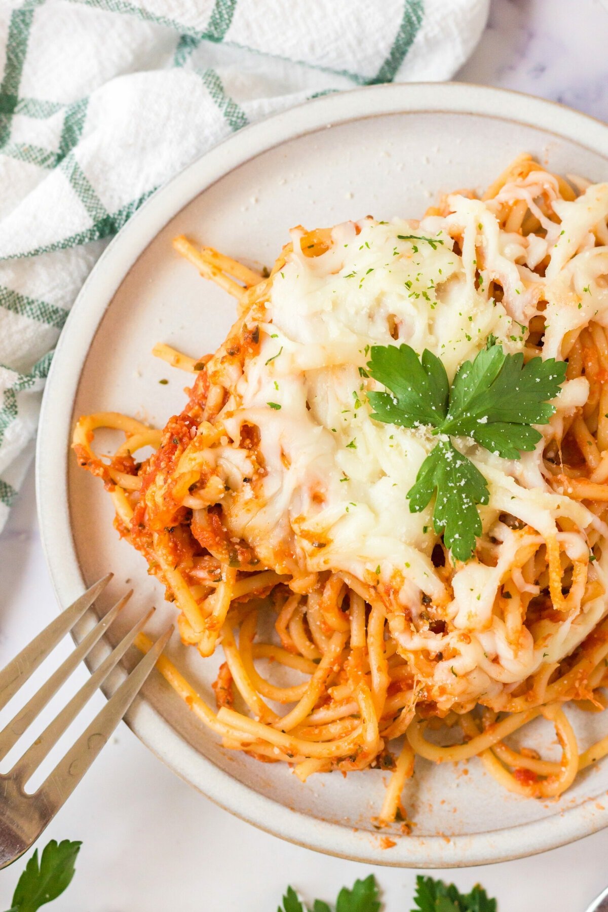 picture of baked spaghetti with melted cheese on a plate topped with basil with forks next to it