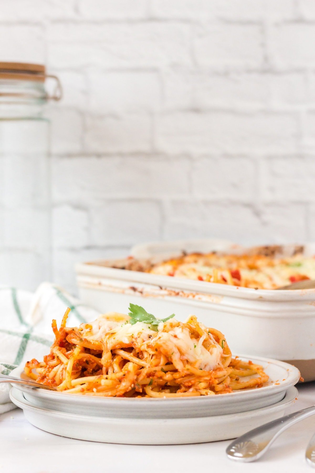 picture of baked spaghetti with melted cheese on a plate topped with basil with forks next to it