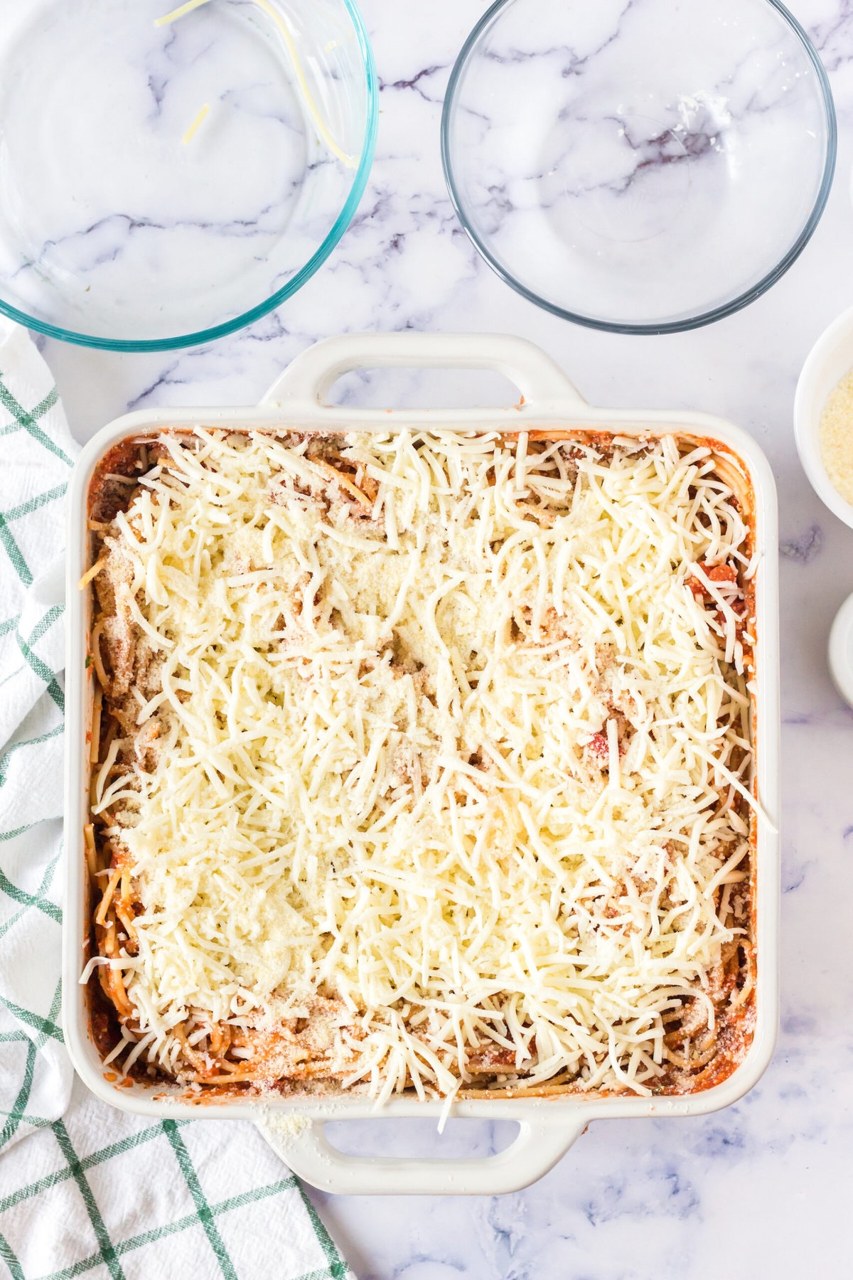 picture of spaghetti in a casserole dish mixed with sauce and covered with shredded cheese