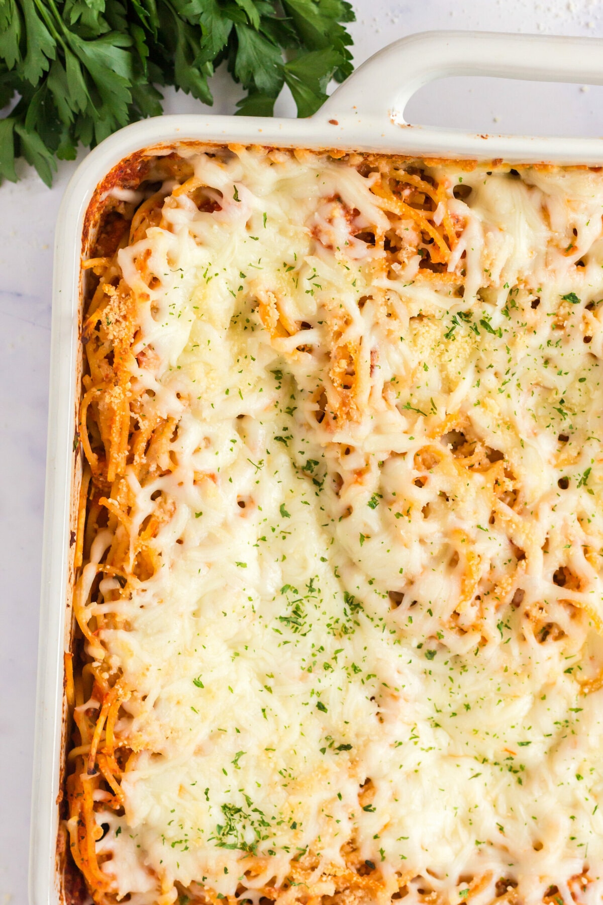 picture of baked spaghetti with melted cheese in a white casserole dish