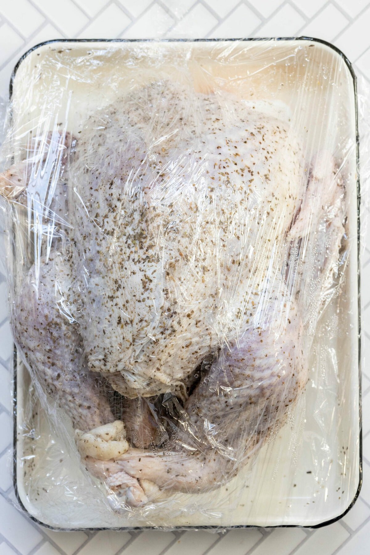 picture of turkey dry brining in plastic wrap on a white tray