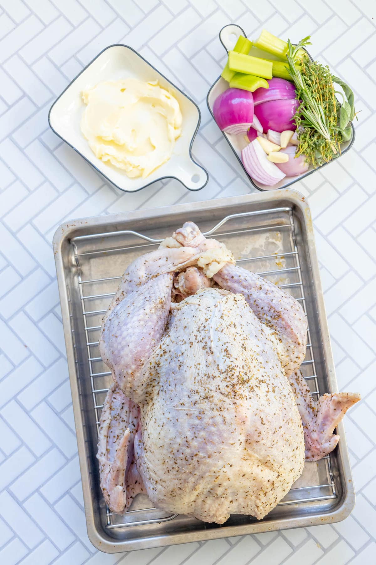 picture of brined turkey next to butter, herbs, chopped onion, softened butter on a table