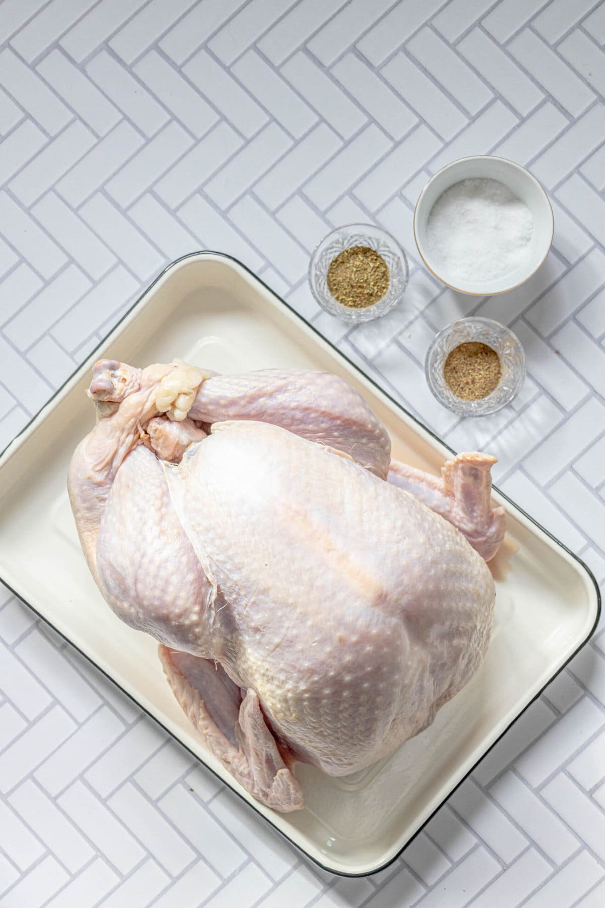 picture of turkey on a tray next to salt, pepper, and herbs
