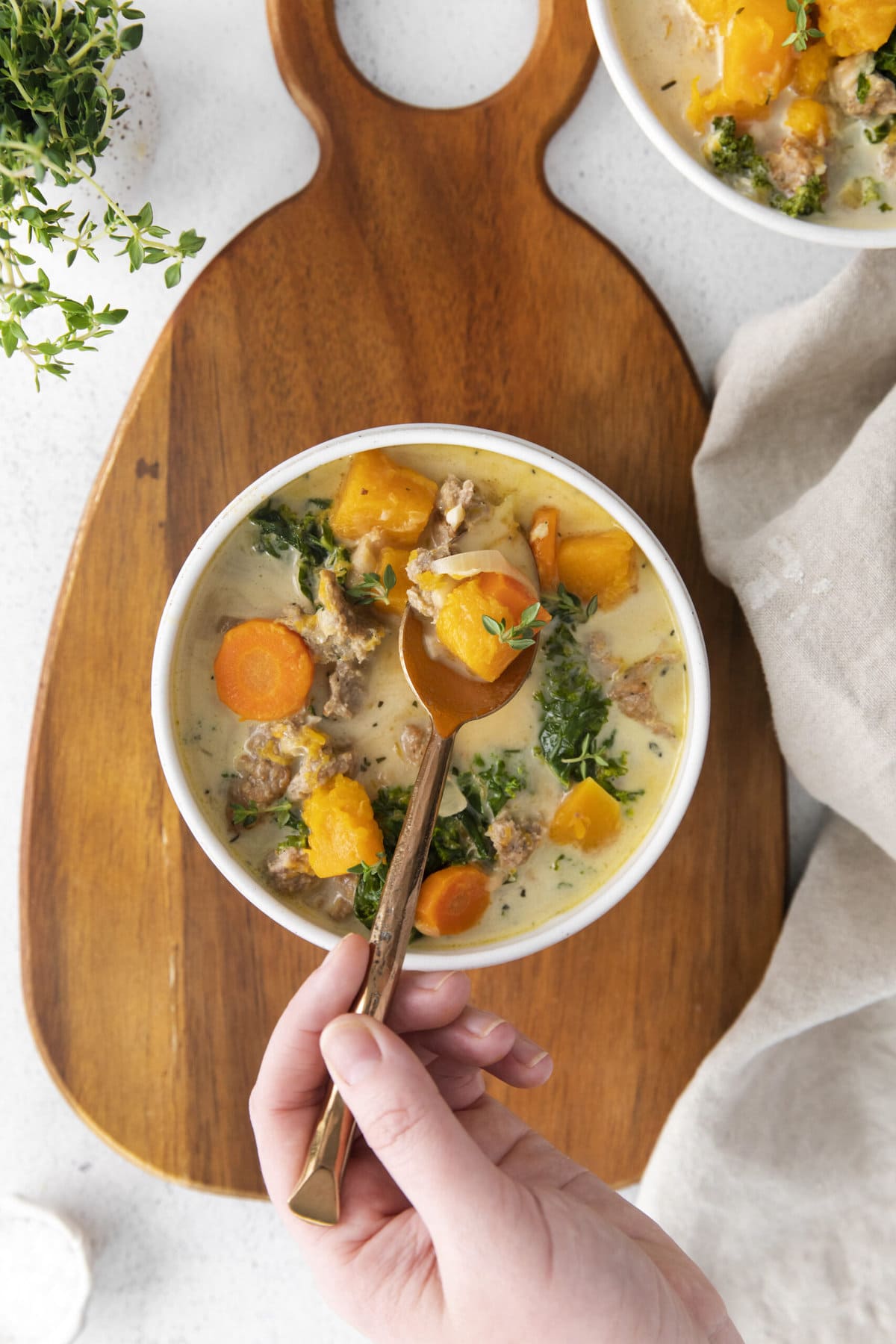 creamy turkey and butternut squash chili with carrots, thyme, kale, and peppers in a white bowl on a table