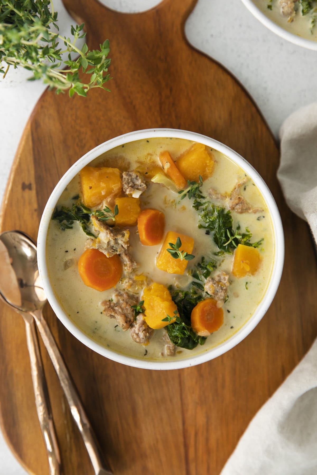 creamy turkey and butternut squash chili with carrots, thyme, kale, and peppers in a white bowl on a table