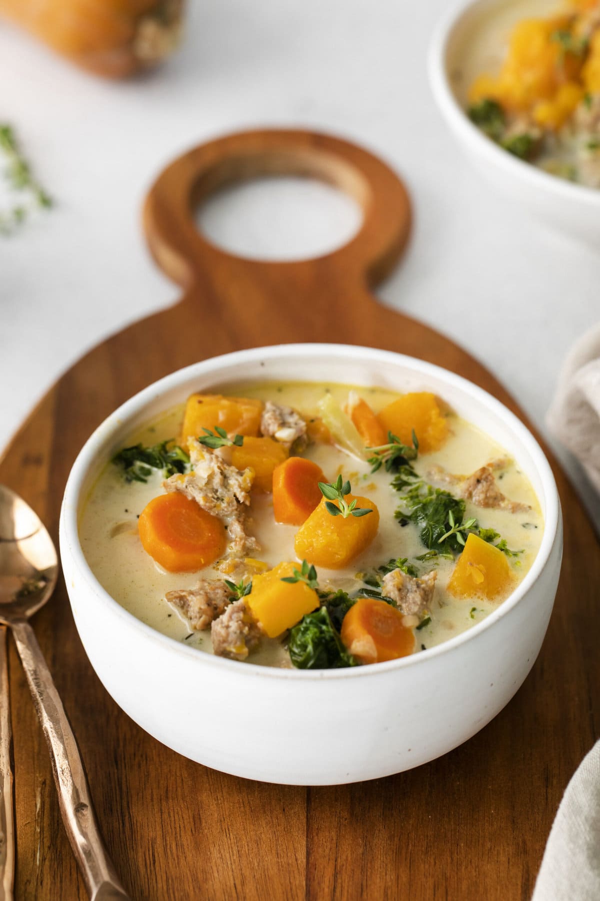 creamy turkey and butternut squash chili with carrots, thyme, kale, and peppers in a white bowl on a table