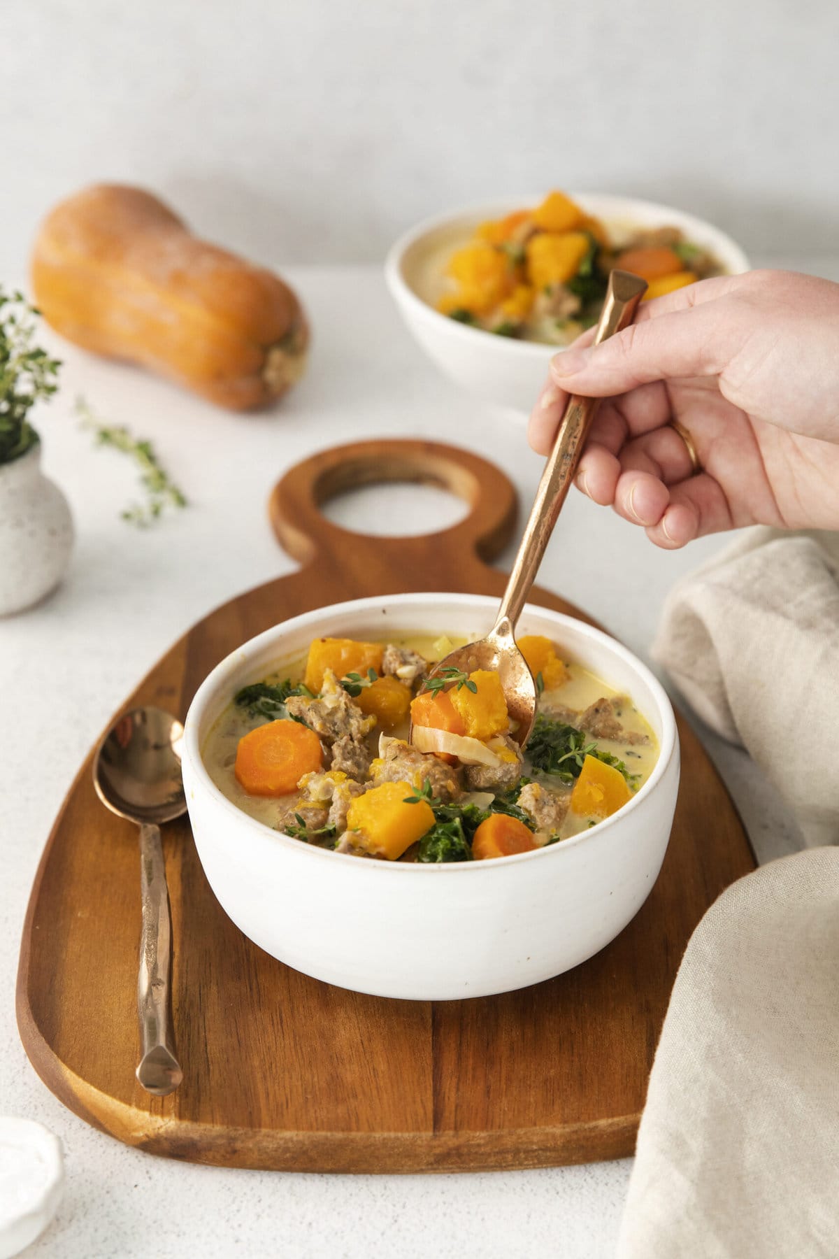 creamy turkey and butternut squash chili with carrots, thyme, kale, and peppers in a white bowl on a table